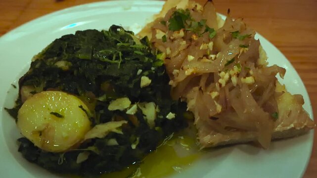 Close up view of a traditional Portuguese codfish dish, bacalhau, served with spinach, potatoes, and onions, drizzled with olive oil on a white plate in a restaurant for a gourmet dinner