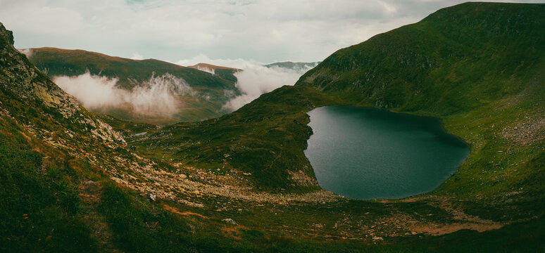Glacial mountain lake with low clouds rolling over a green ridge