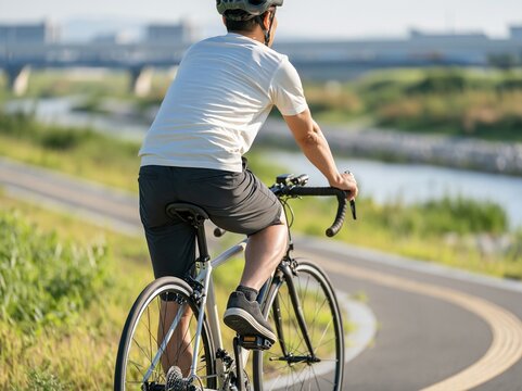 天気の良い川沿いのサイクリングロードを快走する自転車の男性の後ろ姿