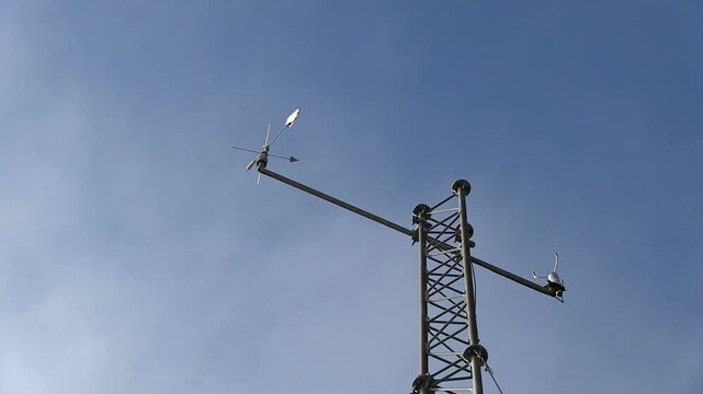 Anemometer measuring wind speed against a clear blue sky, meteorology concept close-up static shot of a cup anemometer and wind vane spinning on a metal mast