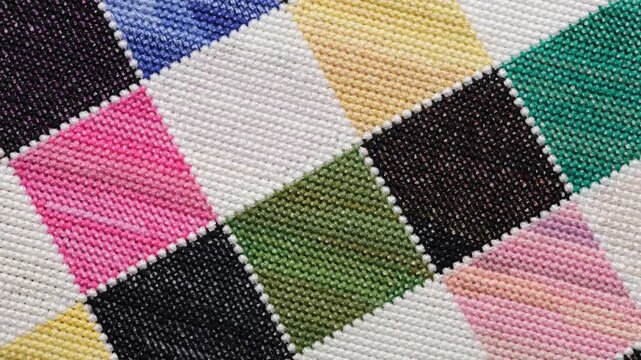 A close-up shot of a colorful checkered pattern hand-embroidered in cross-stitch