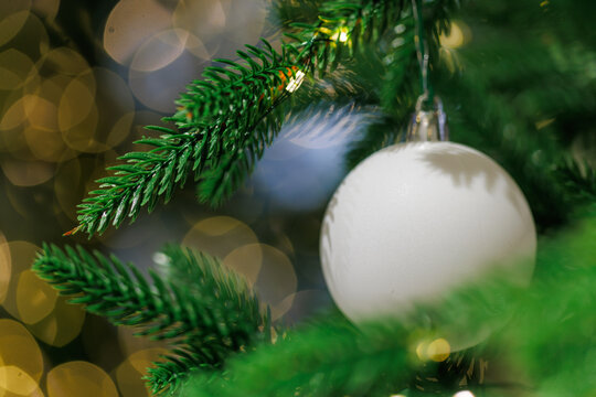 White Christmas ornament on fir tree with golden bokeh lights