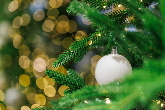White Christmas ornament on fir tree with golden bokeh lights