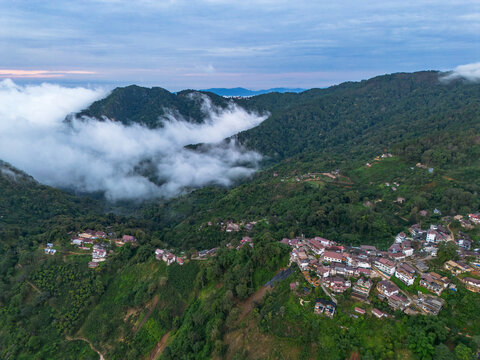 Aerial mountain village landscape northern thailand misty cloud forest hillside panorama with green valley, rural house cluster, winding road, and calm dawn sky