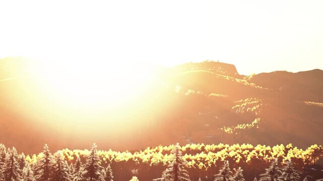 The sun rises above the mountains, illuminating the landscape. Trees stand in the foreground as the light enhances the scenery. This scene captures early morning beauty in nature.