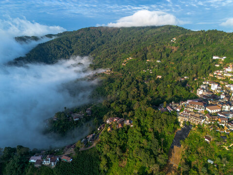 Aerial view mountain village northern thailand forest drifting cloud mist hill valley landscape, scenic rural settlement on green slope with fog and blue sky