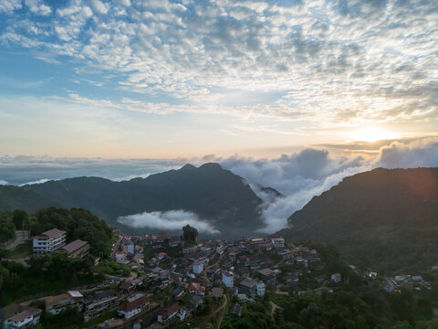 Aerial mountain village sunrise misty ridge forested valley northern thailand with cloud layer above hill, sky, house, and peaceful remote landscape
