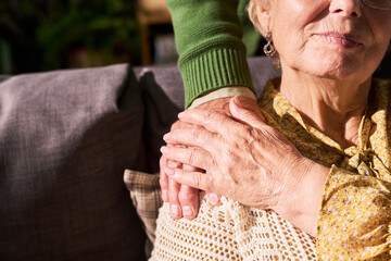 Close up of Caucasian caregiver placing hand on senior woman shoulder supporting her at home....