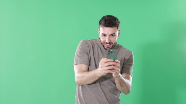 Adult man stands against green screen, holding smartphone up to take photo or scan QR code 