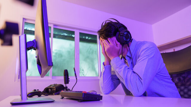 Asian gamer face in hands feeling defeated after losing video game match