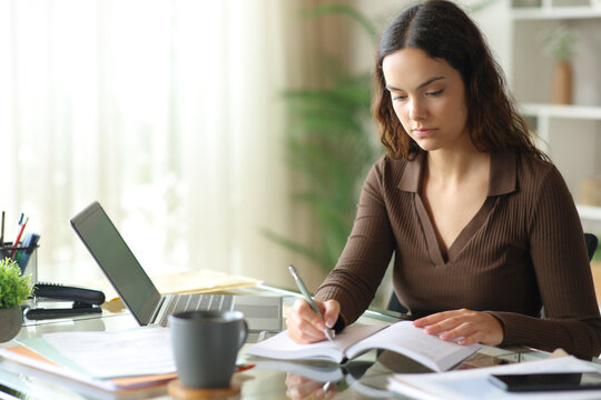 Serious telecommuter writing notes in agenda working online