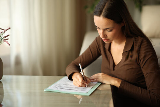 Serious woman is filling out paper form on a coffee table