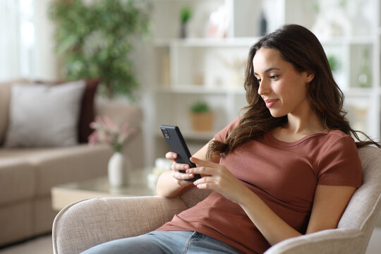 Woman sitting on armchair using cell phone at home