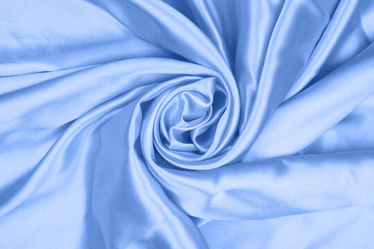 Soft light blue satin silk fabric twisted in a swirl pattern texture background.