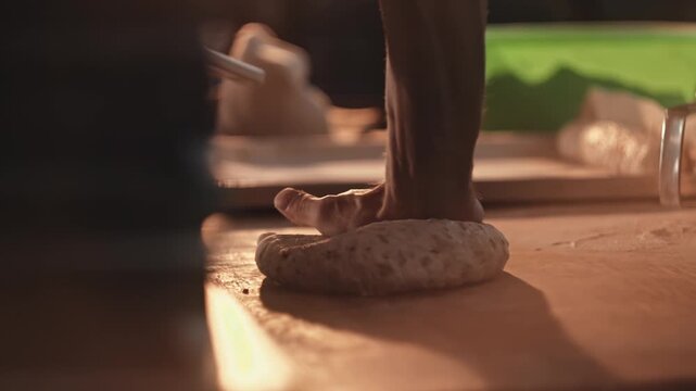 Male Hands shaping dough for bread and rolls production on wooden table inside small bakery. Traditional baking process preparation, culinary craft of artisan baker.