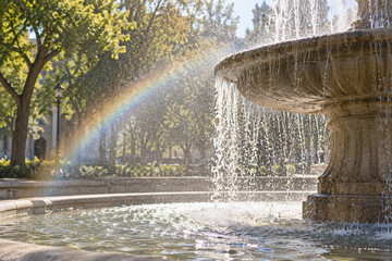 Obraz premium Rainbow forming in the water spray of a sunlit fountain