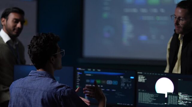 Three engineers gathered at one workstation lean in together as one of them reaches out to point at the result on the monitor inside a dimly lit machine learning startup office.
