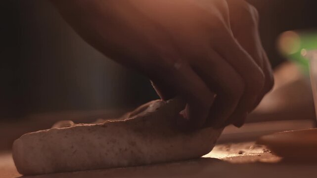 Hands shaping dough into round loaf for baking bread and rolls. Baker working with raw mixture on wooden surface inside small bakery kitchen. Closeup view