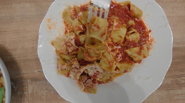 Overhead view of pappardelle pasta in tomato sauce with a fork lifting a bite