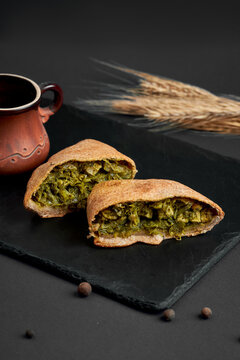 Halved baked samsa pie filled with savory spinach and herbs on black slate board. Delicious vegetarian pastry on dark background.