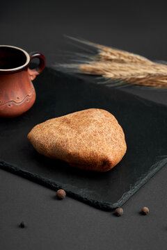 Freshly baked triangular samsa pie with black sesame seeds on slate board. Traditional savory pastry on dark wooden background.