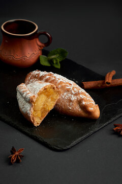 Halved sweet baked pie with cottage cheese and orange filling dusted with powdered sugar on slate board. Dessert pastry on dark background.