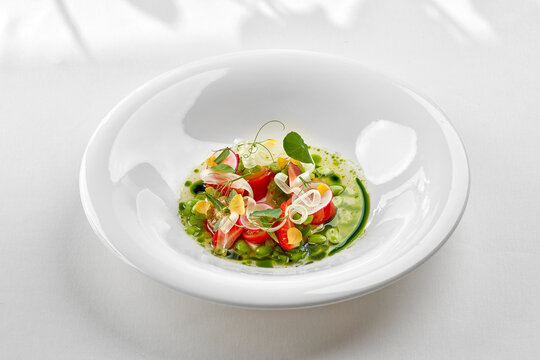 Gourmet summer salad with tomatoes, strawberries, and fresh herbs in a white bowl. Fine dining restaurant dish isolated on white background