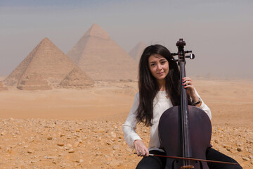 Serene Middle Eastern female cellist seated with cello before the iconic Giza pyramids in an evocative fusion of classical music ancient culture and © .shock