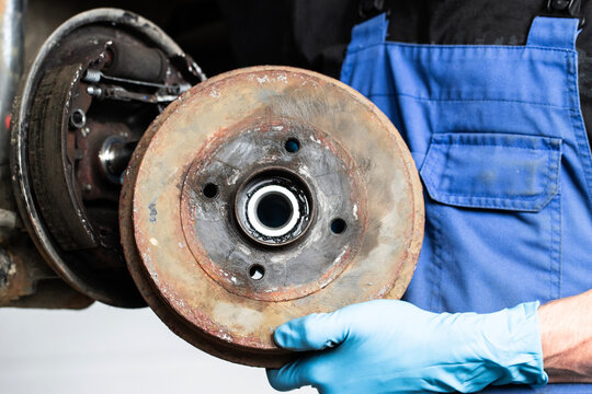A repairman holds a car's brake drum in his hands, replacing brake pads.