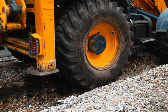 A construction vehicle with large tires is positioned on a gravel surface. The equipment is likely involved in road work or site preparation
