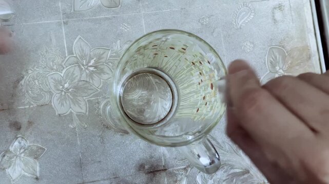 Man opens medicine bag and pours dry mixture into cup. Person prepares beverage, pouring dry white powder into empty glass mug, top-down view preparation. Self-medication at home