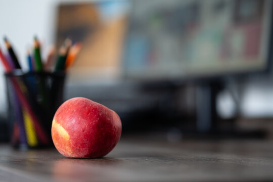 Colored pencils in holder with red apple on desk and blurred computer monitor background for online education concept
