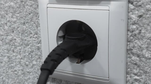 Hand inserting electrical plug into wall socket power outlet and and stick out. Connection device energy supply. Electrical appliance operation concept. Close up view