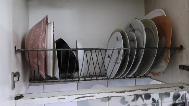 Male hand places clean plates on dish rack shelf in old worn-out soviet kitchen cabinet. Vintage atmosphere, old renovation