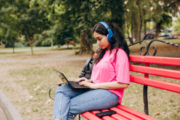 Young woman learning with laptop outdoors on park bench
