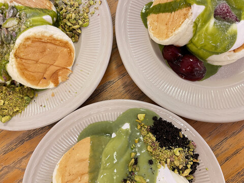 Fluffy Japanese souffle pancakes topped with creamy matcha sauce, whipped cream, berries and nuts on white plates.