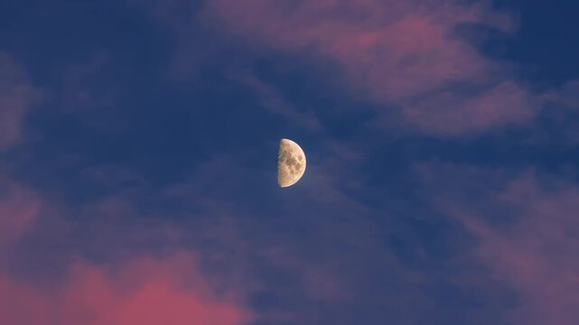 Half moon appearance evening twilight sky with wispy cloud formations. Celestial body glowing deep blue atmosphere. Lunar phase dusk light.