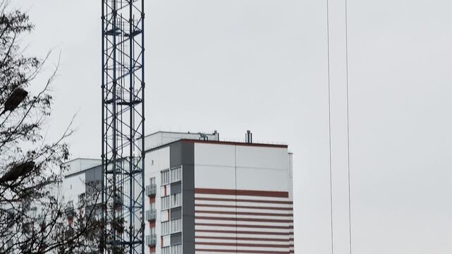 Timelapse sequence of large industrial tower crane assembly showing construction progress near modern residential building against overcast sky with bare tree branches