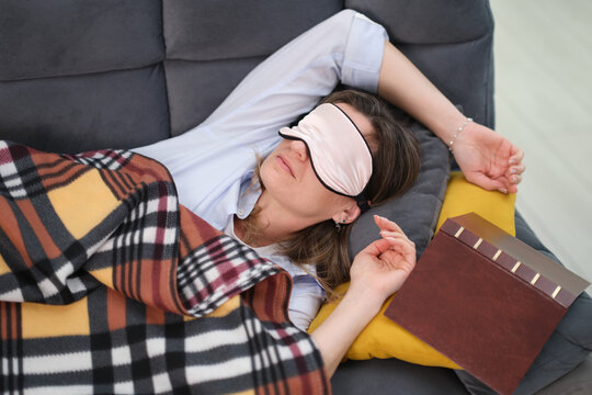 Peaceful woman lies on soft sofa under warm fluffy blanket at home. Comfortable sleep mask covers eyes and female enjoys quiet restful sleep