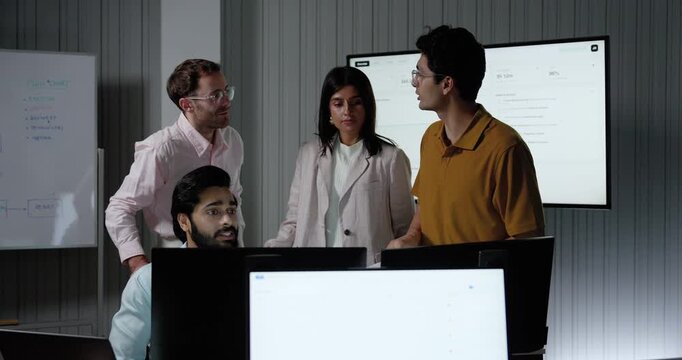 Adult customer support team stands beside seated headset agent, discussing computer information and service workflow while exchanging ideas during collaborative call center briefing in modern office.