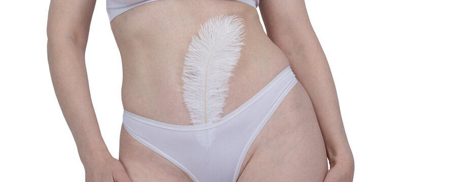 Woman holding soft white feather against smooth skin of bikini area. Concept of gentle hair removal, skincare, depilation and body wellness. Beauty treatment for feminine hygiene