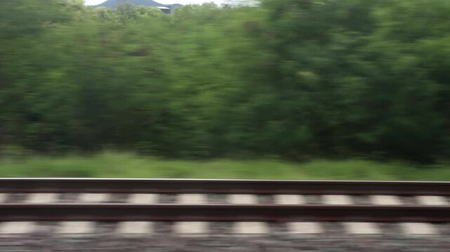 Fast motion blur of railway tracks and green scenery viewed from a moving train window