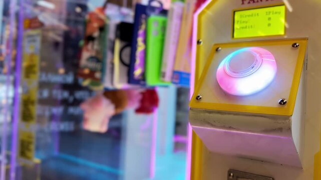 Close up view of glowing play button on arcade claw machine, button changing colors, electronic game cabinet for prize retrieval, fun activity in entertainment center