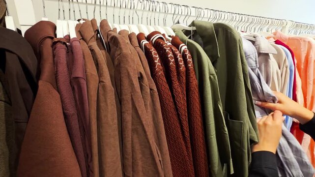 Hand selecting clothing from a retail display rack in a modern apparel store, close up view of garments hanging on hangers, showcasing a shopping experience with various styles and colors for sale