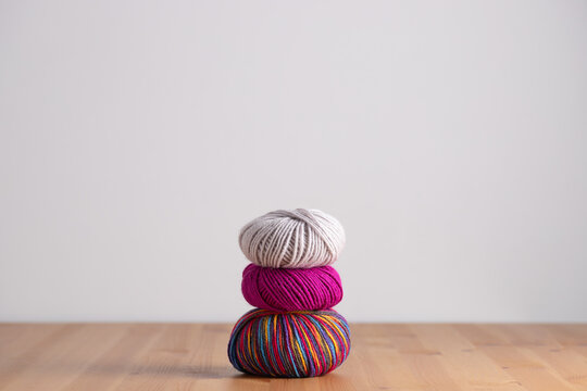 Three yarn balls stacked in different colors on wooden table, horizontal minimalist frame with neutral background and copy space. Concept of creativity and slow living