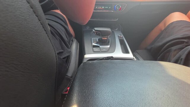 View from back seat of car interior showing driver and front passenger legs with focus on center console gear shifter dashboard controls sun glare creating bright atmospheric effect during travel
