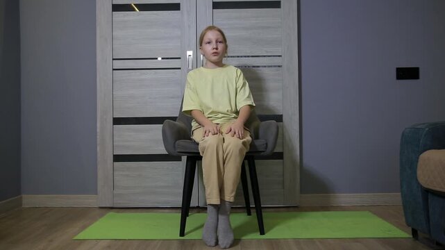 Young girl performing chair exercises at home, focusing on leg movements for fitness and health improvement, an indoor workout routine for children and youth.