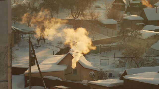 Golden hour illumination of thick smoke plume rising from chimney of house in frosty winter village morning landscape