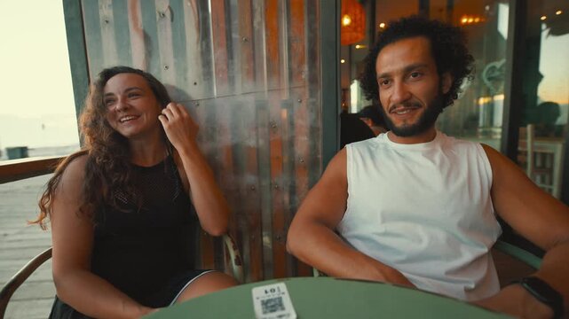Couple talks and enjoys drinks at cafe during sunset by the beach