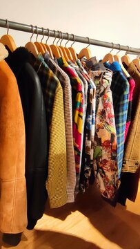 Row of various colorful jackets and coats hanging on wooden hangers along a clothes rack